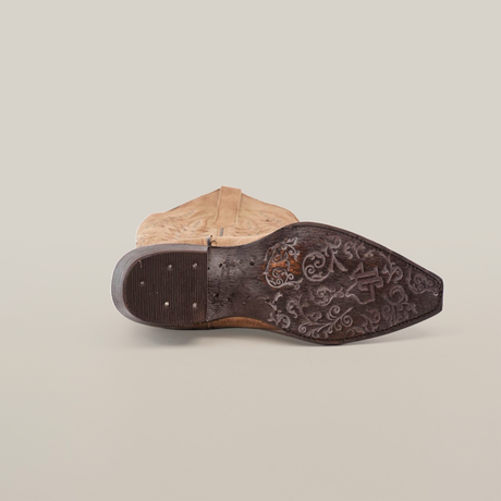 The Madona Sand Suede boot, a tall shaft cowboy style with a snip toe, is shown from the side. Its decorative engravings on the dark brown sole and worn heel with small visible nails are featured against a plain white background.