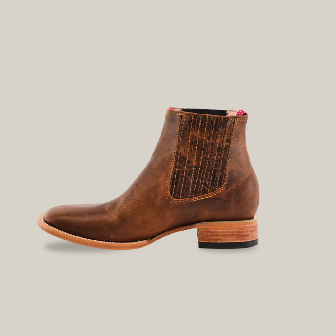 The Avejentado Honey Square Toe ankle boot exudes cowboy elegance with its brown leather, decorative stitching, square toe, and low wooden heel. It features a partially visible interior lining against a white backdrop.