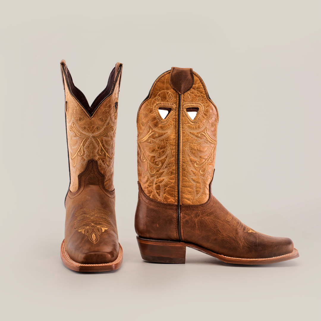 The Western Stitch Camel boots feature premium leather, intricate western stitching, and a narrow square toe. Available in tan and brown with ornate patterns on a short shaft, they boast moderately high heels for an elegant design against a neutral background.