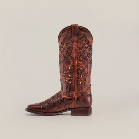 A single Marga Cruz Brick Mid Shaft boot, featuring a square toe design and crafted from premium brown leather with floral stitching and small studs, is set against a plain white backdrop.