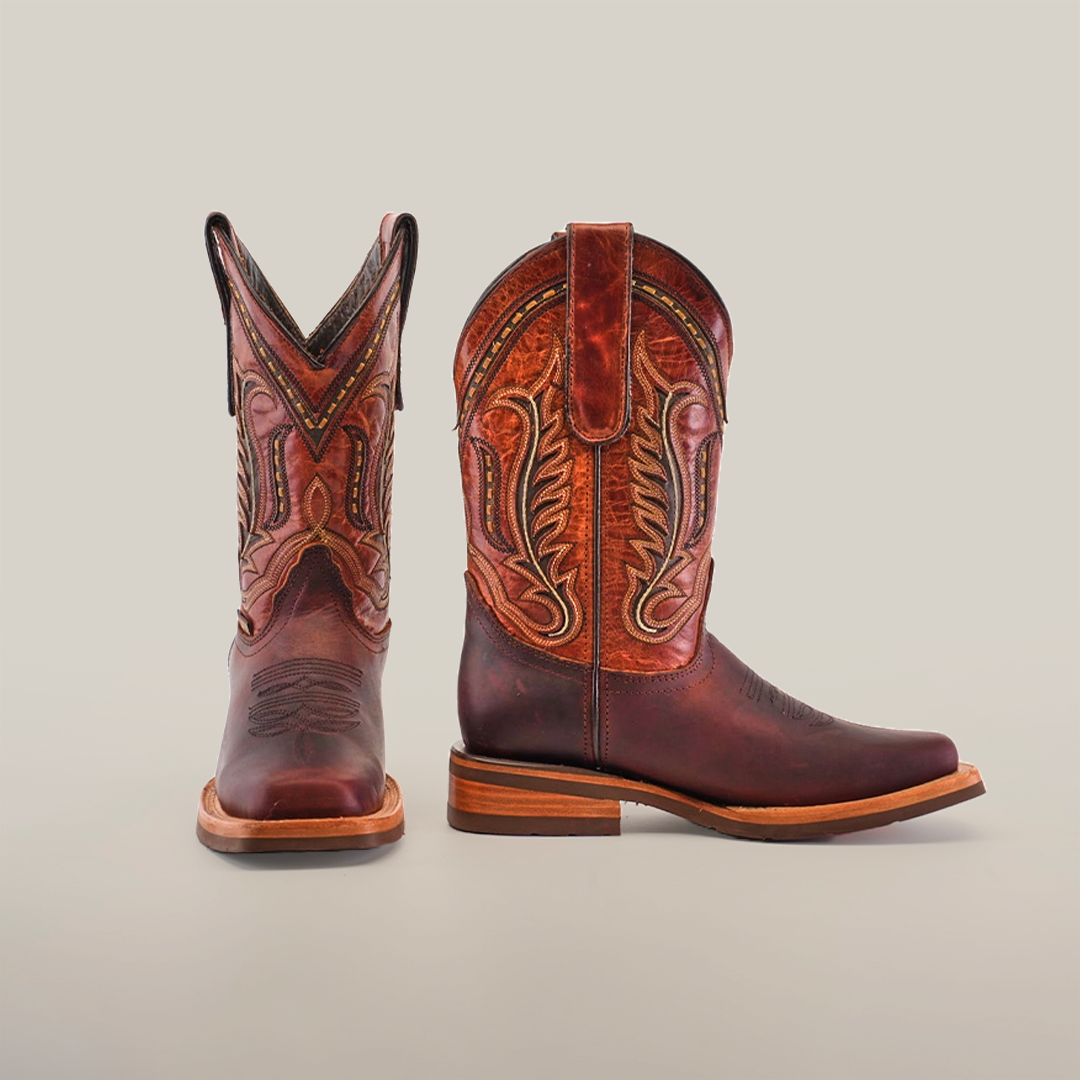 A pair of brown Azkar Moka Slip Resistant Sole Rodeo Toe cowboy boots with intricate stitching. The left boot is upright, and the right boot is slightly angled. With a wooden heel, these stylish boots are set against a plain white background.