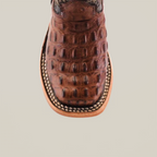 A detailed view of the Caiman Hornback Print Chocolate Square Toe cowboy boot highlights its Western style with a textured reptile pattern, intricate stitching on the leather toe, and a sturdy sole set against a plain white background.