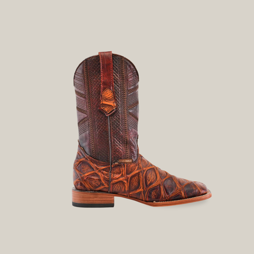 A single Big Bass Pirarucu Print Rustic Cogñac cowboy boot, featuring a textured reptile-like design, flat heel, and pull straps on the sides, is displayed against a plain white background.