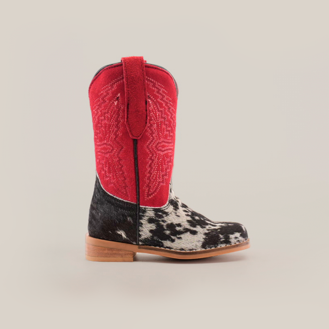 The Cowhide Hair Pinto Square Toe boot boasts a red upper with intricate stitching and a black and white cowhide pattern on the lower section. It features a square toe design resting on a sturdy brown sole, displayed against a plain white background.