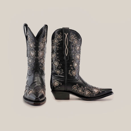 Explore the Studded Hearts Black - Short Shaft - Snip Toe boots, a luxury bootmaking marvel. Handcrafted with intricate silver embroidery featuring heart and floral designs, one boot stands upright while the other is angled to highlight its exquisite side details.