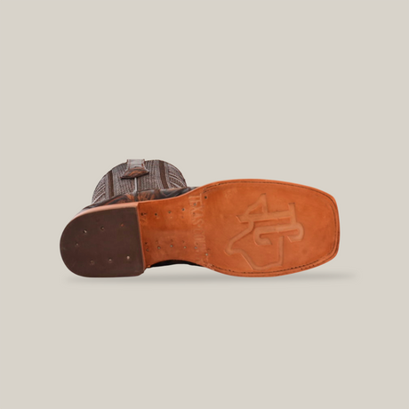 Bottom view of the Big Bass Pirarucu Print Rustic Brown - Square Toe boot reveals a tan leather sole with an embossed logo, a dark brown heel, and a textured upper in a striking pirarucu pattern.