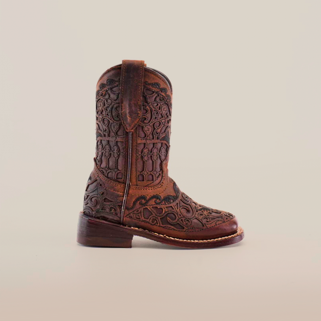 The Taurine Matte Chocolate Square Toe boots feature intricate floral and geometric patterns etched into premium leather, showcasing western elegance. The ornate design highlights exceptional craftsmanship against a light background, making these boots a classic choice.