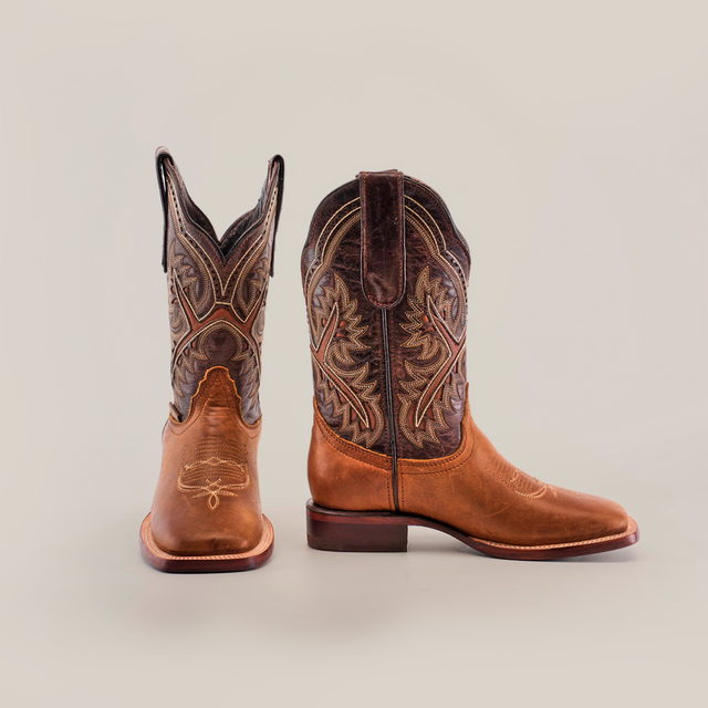 A pair of Cater Honey Square Toe boots, crafted from premium leather with detailed brown and tan stitching, is displayed on a white background. One boot stands while the other tilts, showcasing the superior craftsmanship and intricate embroidery around the shaft.