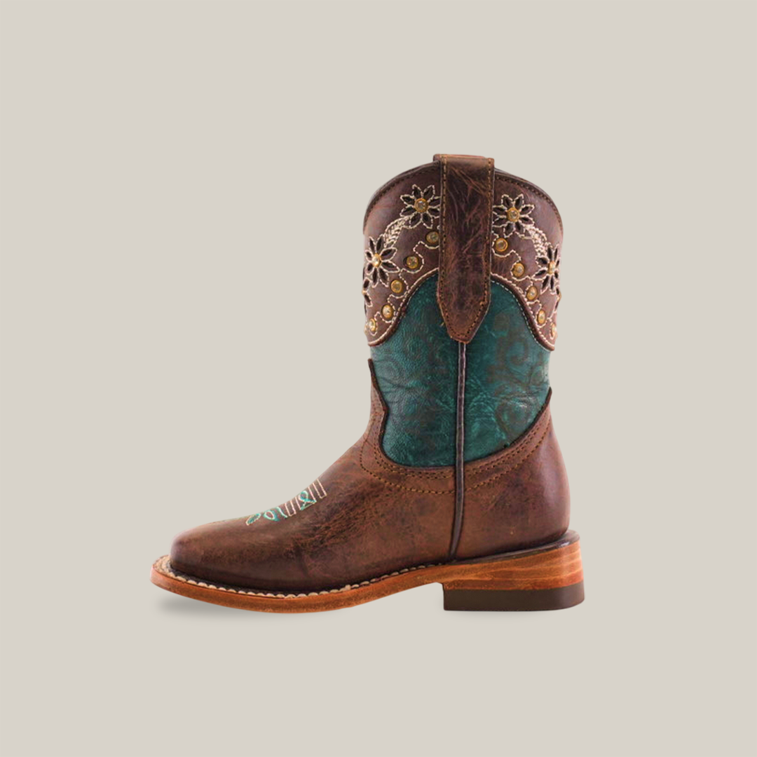 The Grecas Tabaco - Square Toe is a premium leather brown cowboy boot, featuring intricate floral embroidery and turquoise detailing on the shaft. Its smooth texture, low heel, and sole stitching blend rustic charm with colorful elements through traditional craftsmanship.