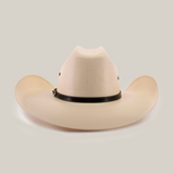 The 500X Bull Straw Hat embodies Western elegance with its cream color, wide brim, and tall pinched crown. Accented by a genuine leather band at the crowns base, it rests gracefully on a plain white background.