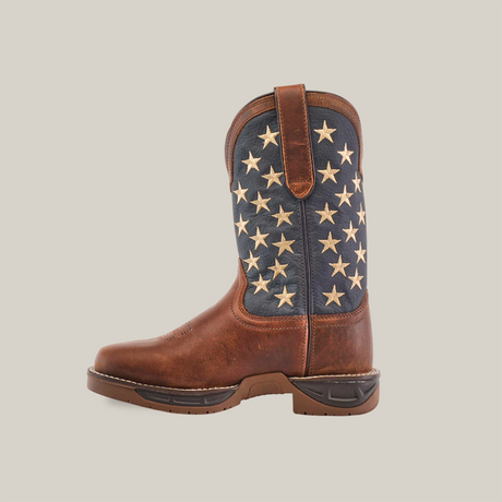 The Navy Brown US Flag cowboy boot features premium cowhide leather with a brown foot and shaft, a blue upper adorned with rows of cream stars, and a durable sole. Highlighted against a plain white background, it offers waterproof protection with a soft toe for comfort.