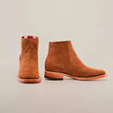 Two Prime Suede Caramel Square Toe ankle boots are displayed, one facing forward and the other showing the side, on a plain white background. They feature brown suede with classic design, wooden sole, elastic side panels, and a subtle square toe charm.