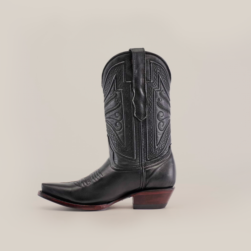 The Plane Jane Black- Short Shaft - Snip Toe boot, made from premium leather, features detailed stitching and a pointed toe. Set against a white backdrop, it has a low wooden heel and decorative shaft patterns, exuding Western artistry.
