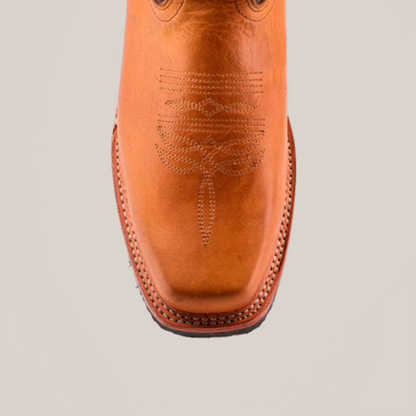 Close-up of the Cater Honey rodeo toe boot, crafted from premium cowhide leather with intricate stitching on the square toe, featuring visible stitching around the slip-resistant sole, set against a plain white background.