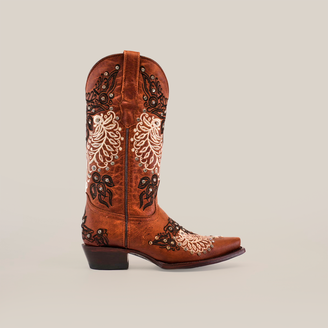 The Faenza Crystals Tabaco boot, with a mid shaft and snip toe, features intricate white and black floral embroidery on brown leather against a white background. It includes delicate crystal embellishments, providing elegance atop its pointed toe and low heel.