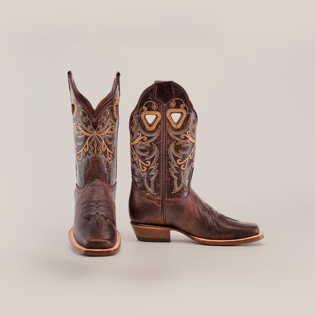 The Western Stitch Tabaco Short Shaft boots, made from premium leather, showcase detailed yellow embroidery and narrow square toes. They feature a stacked heel and decorative cutouts, with the brown cowboy boots set against a plain white background.