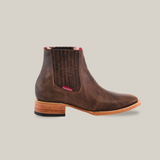 The Alamo Brown Square Toe Ankle Boot, crafted in brown leather, features a stacked wooden heel and embodies Western fashion. It includes elastic side panels for easy slip-on, a red side tag, and a black rubber heel section for enhanced grip.