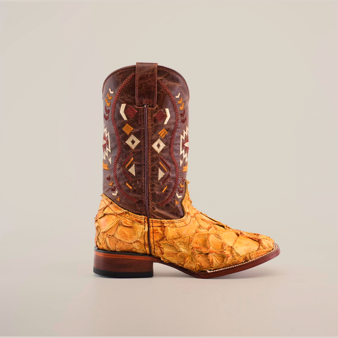 The Exotic Pirarucu Fish Patchwork Honey Square Toe boot features a yellow-textured lower section mimicking fish scales and a dark brown leather upper with geometric white and brown patterns. Its presented standing against a clean white background.