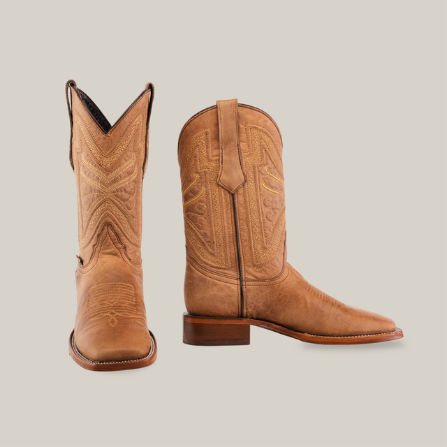 Two Sierra Fawn - Square Toe cowboy boots in tan, crafted from premium cowhide leather, showcase intricate stitching. One boot stands upright and the other tilts forward slightly, highlighting its toe and side details against a plain white backdrop.