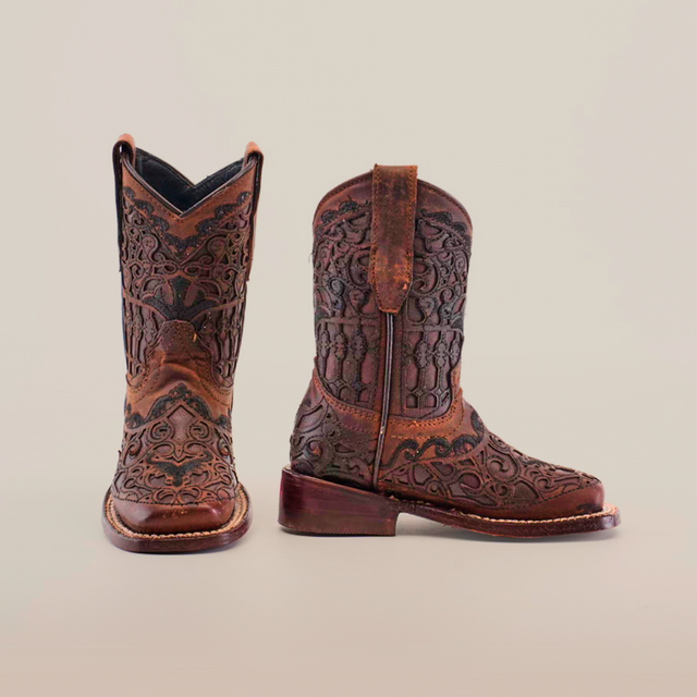 The Taurine Matte Chocolate Square Toe boots highlight premium leather craftsmanship with intricate brown leather patterns. The left boot is front-facing, the right side-facing, radiating western elegance against a plain white backdrop.