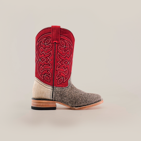 The Cowhide Hair Pinto Square Toe boot features a red upper with intricate embroidery, a cowhide design in the midsection, and a tan leather sole with a black heel. It has a stylish square toe and stands upright in well-lit settings.