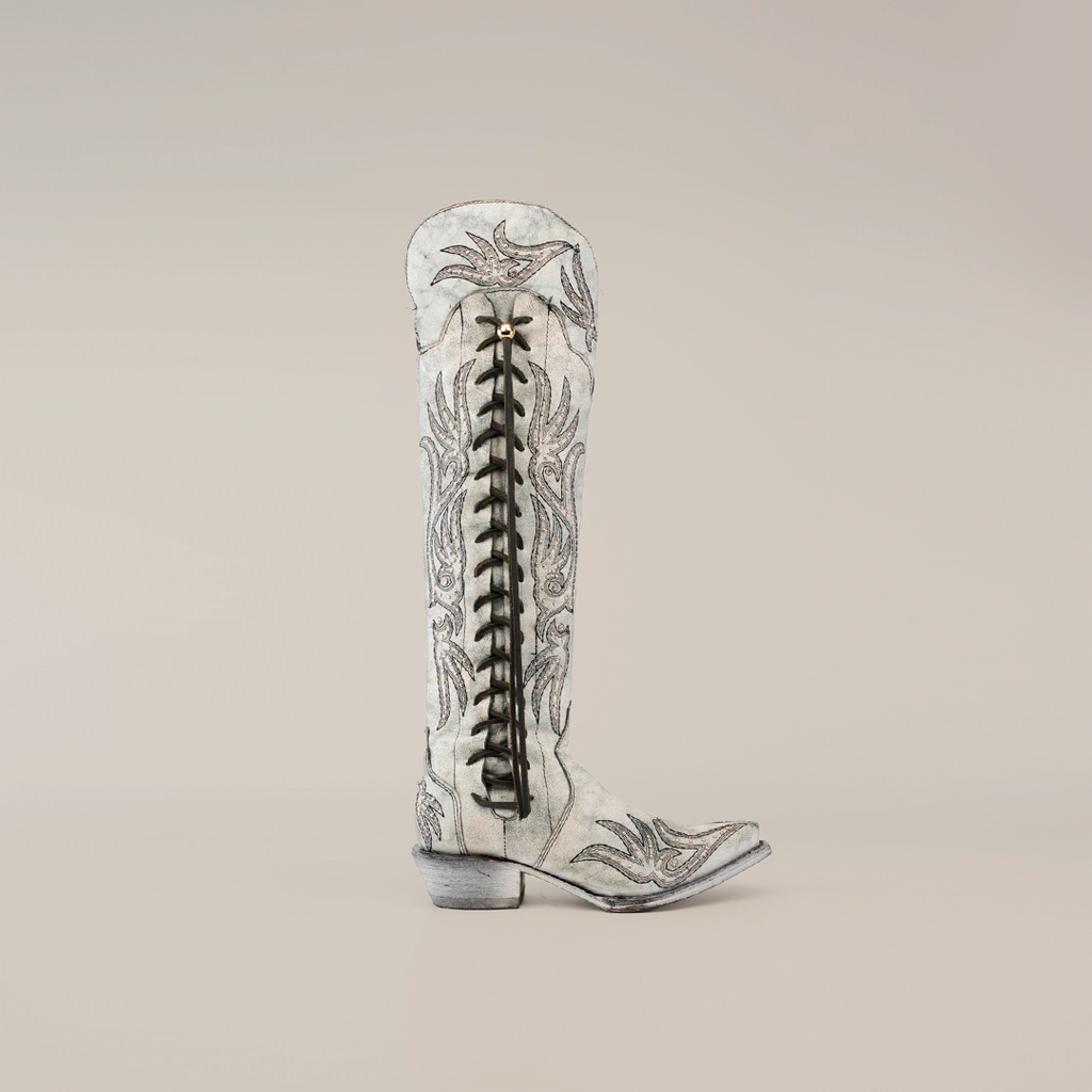 The Emma Alaska Black boot features a tall shaft with intricate decorative stitching on light gray, a prominent black vertical zipper, pointed toe, and low heel, embodying Western heritage.