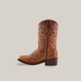 The Carola Tabaco - Snip Toe boot is a single brown cowboy boot made of premium leather, adorned with detailed white embroidery on the shaft and foot. It features a low heel and pull straps on either side, set against a simple white background.