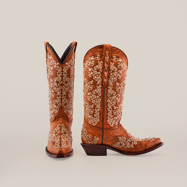 A pair of Cleo Honey Crystals cowboy boots features intricate white embroidery on rich brown leather. Styled in Western flair, one boot is positioned forward while the other is angled from the side, all set against a plain white background.