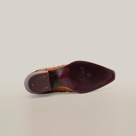 The image features the brown sole of a Cotulla Fawn Crystals - Short Shaft - Snip Toe shoe, embodying luxury craftsmanship. The dark burgundy sole, with embossed text and decorations, represents Western fashion. Positioned sideways on a white background, it emphasizes detailed heel intricacies.