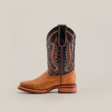 The Cater Honey Slip Resistant Sole Rodeo Toe boot features a brown cowboy design with decorative patterns on the dark leather shaft, a Rodeo toe, and a stacked heel. Made from premium leather, it includes a slip-resistant sole and pull strap, showcased against a white background.