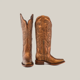 The Eden Copper Tall Shaft boots, with a narrow square toe, showcase intricate brown leather embroidery and a side zipper. One boot stands upright while the other is angled side-on, highlighting their luxury craftsmanship and block heel design.