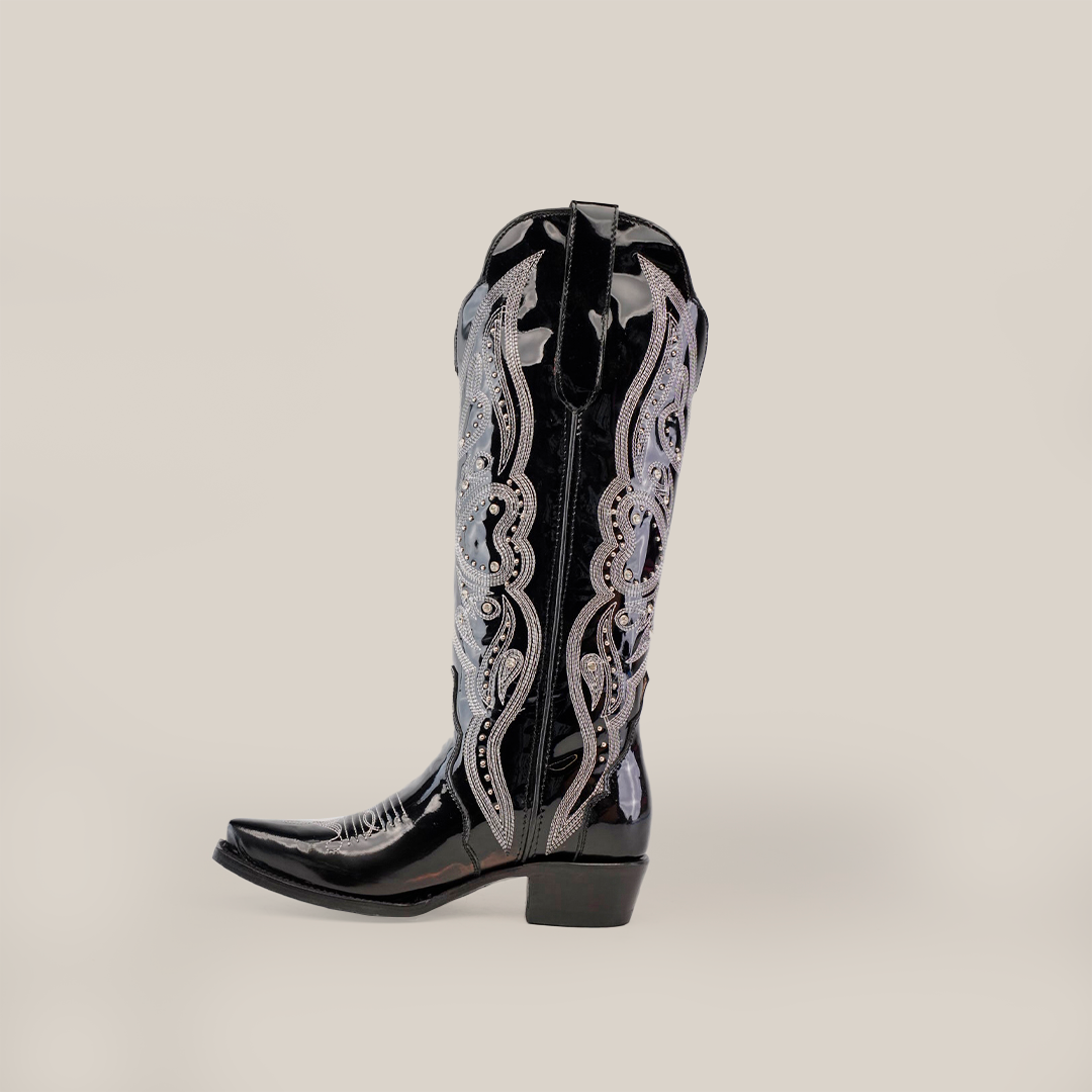 The Artemisa Patent Black cowboy boot features premium leather, intricate silver embroidery, a pointed snip toe, and a low block heel, photographed against a plain background.