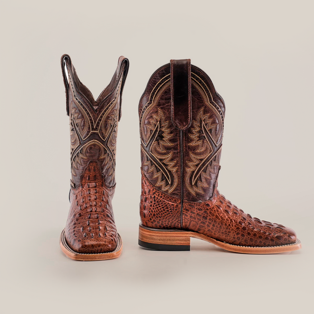 Two luxury cowboy boots crafted from textured brown leather with intricate stitching are shown against a white background. One features more embossing, while both have pull straps, wooden heels, and the elegant Caiman Hornback Print Chocolate Square Toe design.