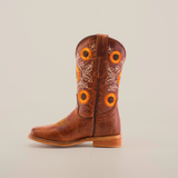 The Sunflowers Tabaco - Square Toe cowboy boot boasts exquisite sunflower and leaf embroidery on the shaft. It features a wooden heel and stitched square toe, all against a plain white background, accentuating its premium leather finish and superior craftsmanship.