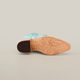 The image displays the sole of an Amara BB Suede-Tall Shaft-Snip Toe boot in light turquoise suede leather resting on its side, featuring a tan sole with intricate floral engravings and a decorative design near the pointed toe.