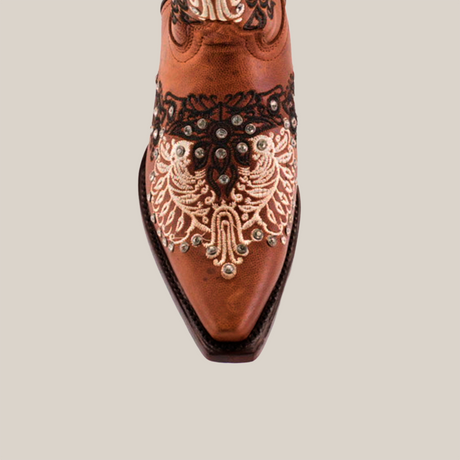 The Faenza Crystals Tabaco boots feature a close-up of a handcrafted brown cowboy style with intricate black and white embroidery and shiny studs on the toe. Flaunting floral and paisley patterns, their ornate leather adds elegance to any outfit.