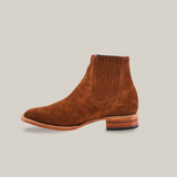 The Prime Suede Caramel Square Toe is a brown suede ankle boot featuring a wooden heel and elastic side panels, offering a touch of Western style, shown against a white background.