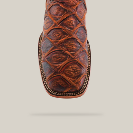 Close-up of the Big Bass Pirarucu Print Rustic Cogñac - Square Toe cowboy boot, highlighting intricately textured leather with detailed stitching and a decorative pattern reminiscent of pirarucu print on the upper against a plain white background.