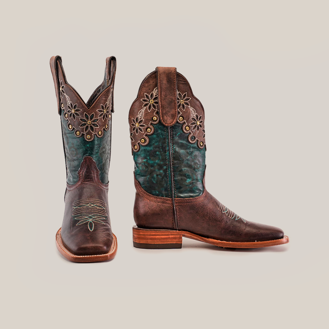 A pair of Grecas Brown - Short Shaft - Square Toe boots features teal accents and floral embroidery on the shaft. One boot is angled forward, the other side-on, highlighting the wooden heel and intricate stitching, showcasing luxury western footwear at its finest.