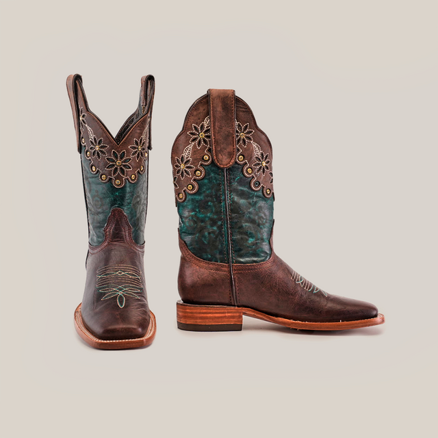 A pair of Grecas Brown - Short Shaft - Square Toe boots features teal accents and floral embroidery on the shaft. One boot is angled forward, the other side-on, highlighting the wooden heel and intricate stitching, showcasing luxury western footwear at its finest.