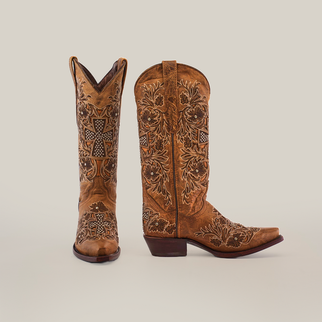 The Alamo Camel Crystals, mid-shaft snip-toe boots, exhibit artisanal craftsmanship with intricate floral and cross designs on a white background. One boot faces forward and the other from the side, showcasing embroidery and stitching details. Perfect as unique womens boots.