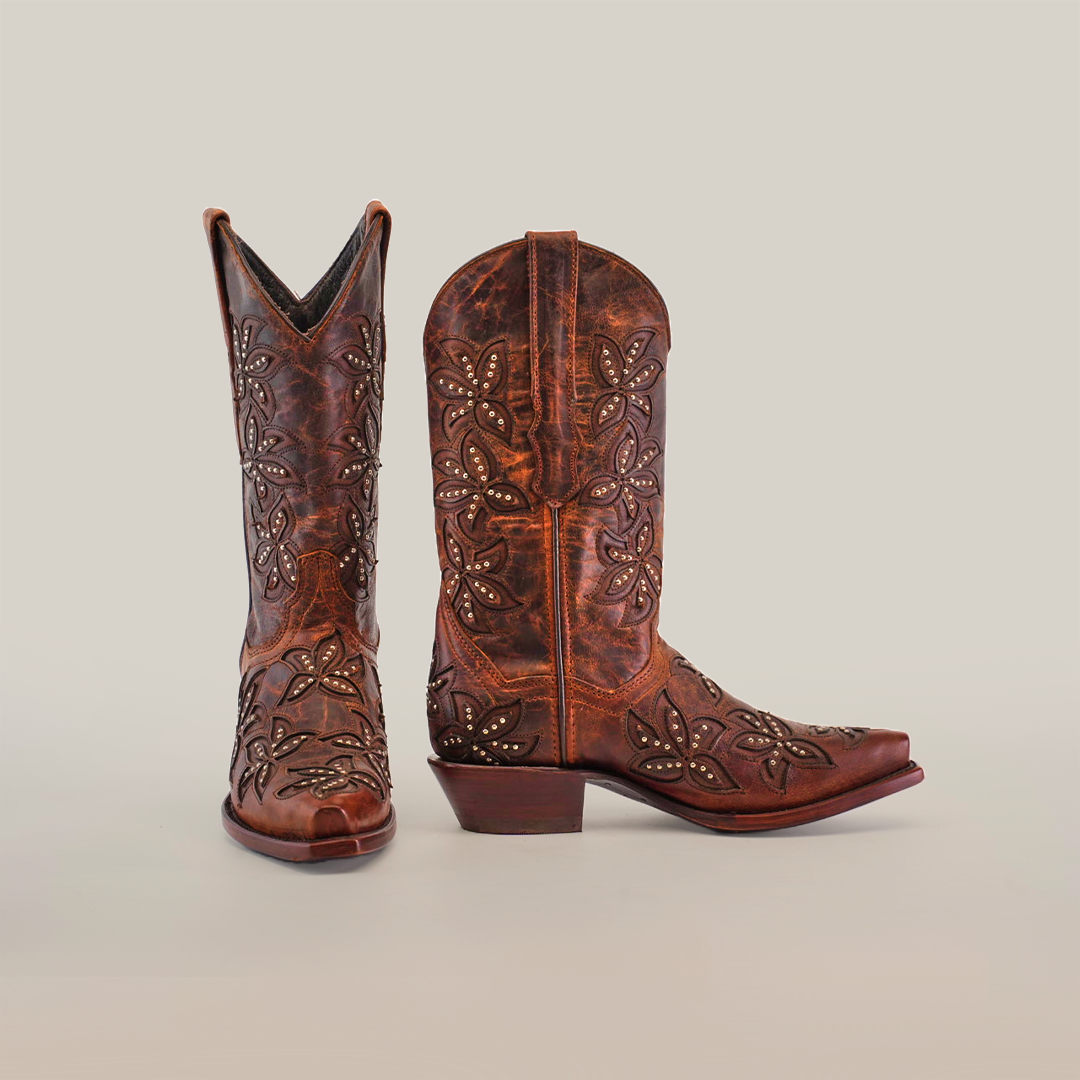 The Cosala Moka - Mid Shaft - Snip Toe women’s cowboy boots feature premium brown leather with decorative floral embroidery and metal studs. One boot stands upright while the other is angled, highlighting the handcrafted details against a plain white background.