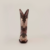 The Faenza Crystals Brown boot, featuring a mid shaft and narrow square toe, stands on a plain white background. Crafted from premium leather, it showcases intricate white floral embroidery and gold accents for an elegant touch to the rugged design.