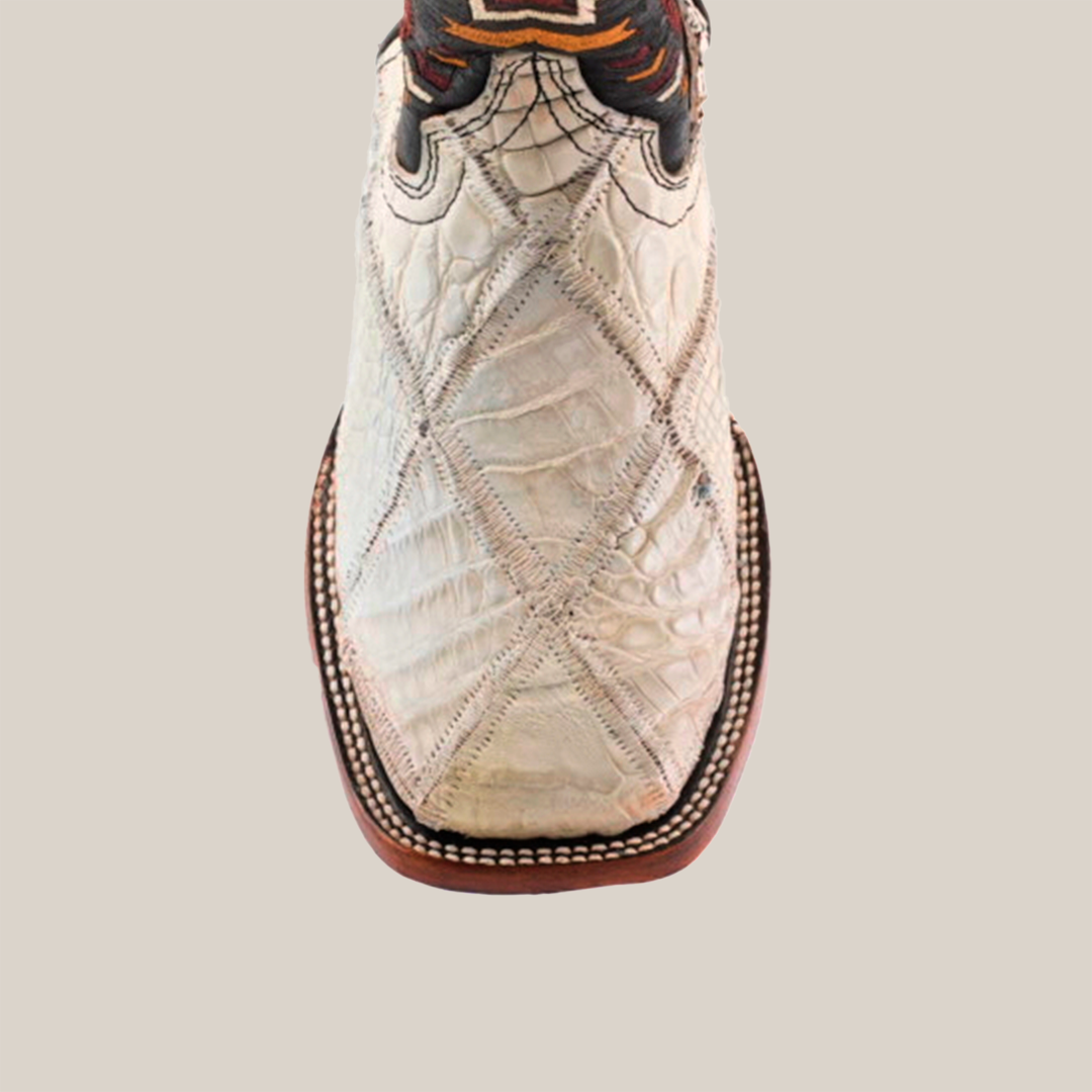 Close-up of the Exotic American Alligator Patchwork Bone Square Toe boot, showcasing its white square toe crafted from textured leather with intricate patchwork stitching in dark and light threads. A brown sole complements it, along with decorative elements near the top.