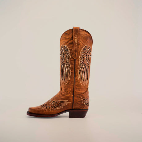 The Texas Cross Glitterbomb Camel showcases a premium leather cowboy boot with decorative wing patterns and chic glitter details on its narrow square toe. The elegant brown boot is set against a white backdrop, emphasizing its rugged charm.