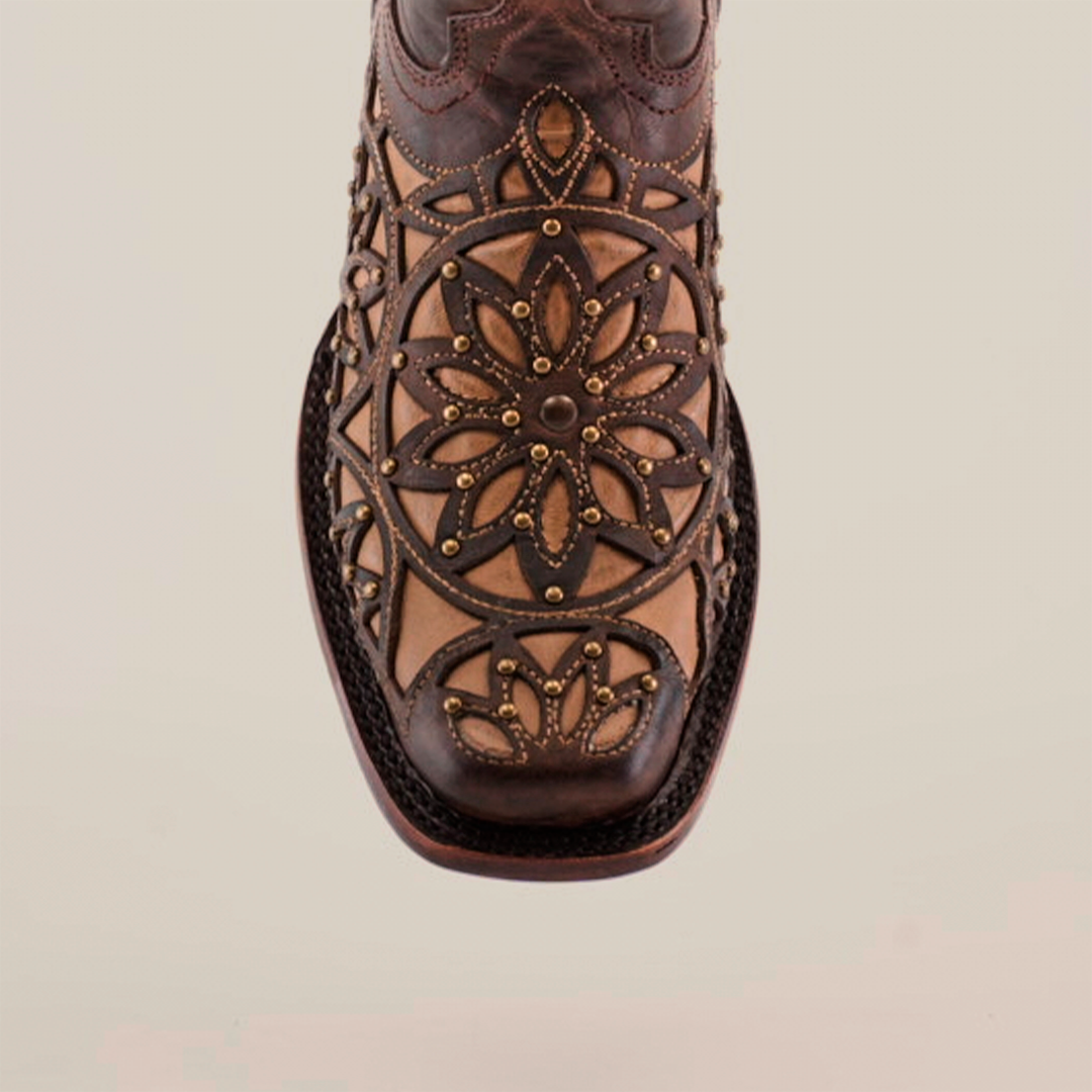 Close-up of handcrafted Vitralli Studs Tabaco boots highlighting intricate floral and geometric patterns on the toe, blending dark and light brown tones. Crafted from premium leather with decorative stitching, these mid-shaft boots feature a narrow square-shaped toe design.