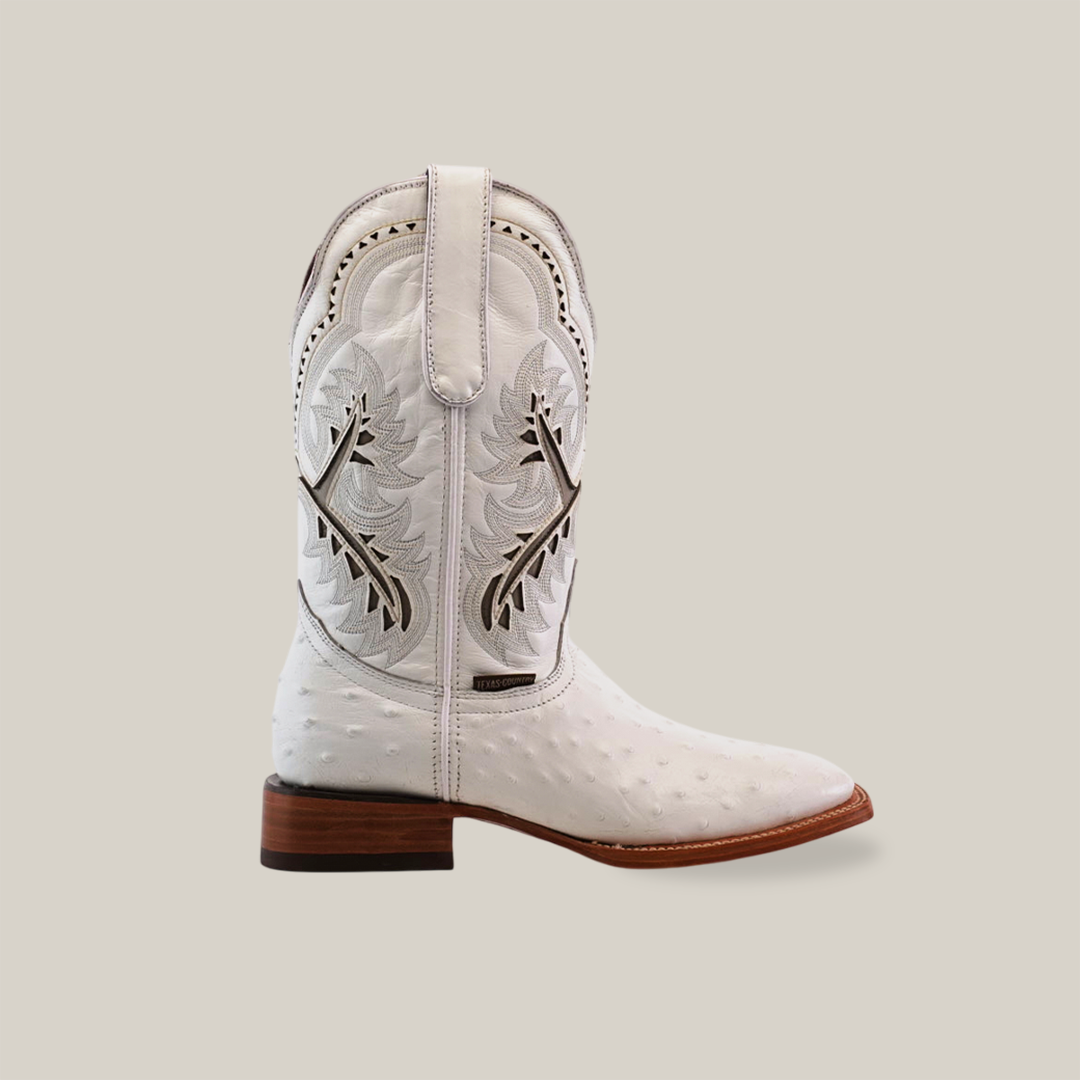 The Karoo Ostrich Print White - Square Toe boot is crafted from premium cowhide leather, showcasing detailed stitched leaf patterns on the shaft. It features a square toe and a contrasting brown wooden heel, all set against a plain white background.