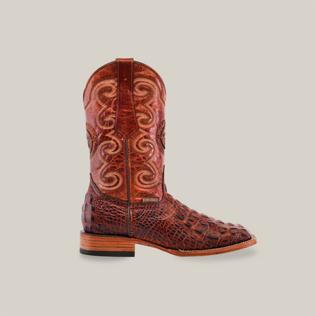 The Morelet Crocodile Print Cogñac boot boasts intricate brown cowhide leather patterns and a textured crocodile-print square toe. It features a flat wooden heel, tall shaft with decorative swirls, and its exquisite details stand out against the white background.