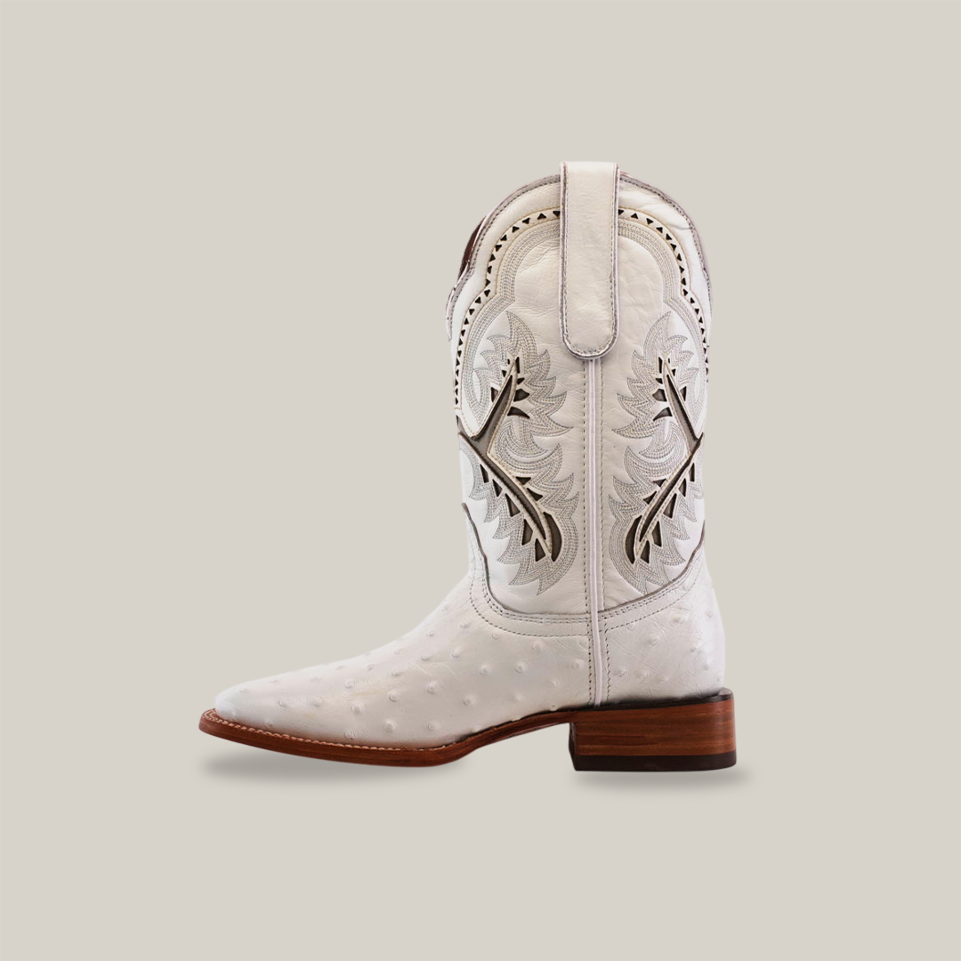 The Karoo Ostrich Print White boot boasts a premium cowhide leather texture with intricate stitched designs, decorative cutouts, and patterns. It features a square toe and wooden heel, set against a plain white background for an elegant look.